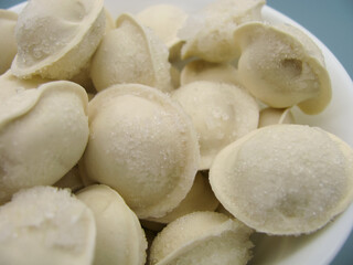 Fototapeta na wymiar Frozen store-bought dumplings in a white bowl on a blue background.
