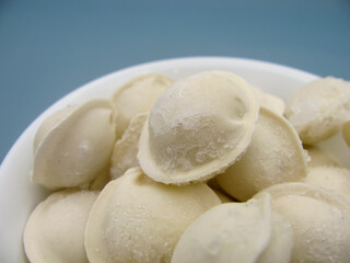Fototapeta na wymiar Frozen store-bought dumplings in a white bowl on a blue background.