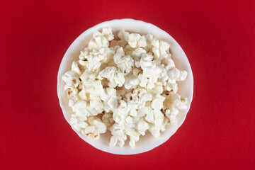 Popcorn in a white bowl on a red background. View from above.