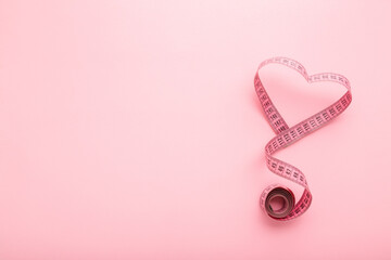 Heart shape created from rolled out measure tape on light pink table background. Pastel color. Closeup. Empty place for text. Top down view.
