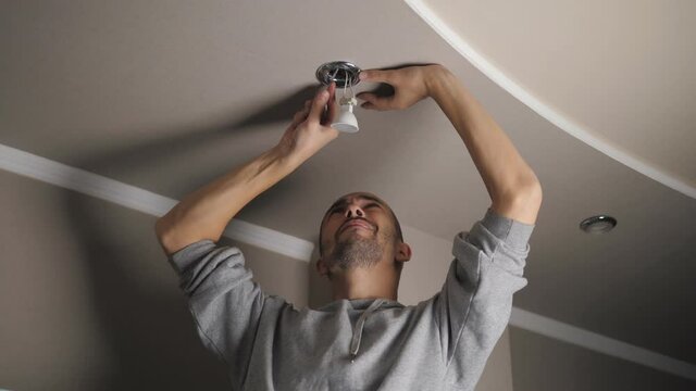 A young man is repairing a ceiling soffit. Replacing the LED lamp at the downlight