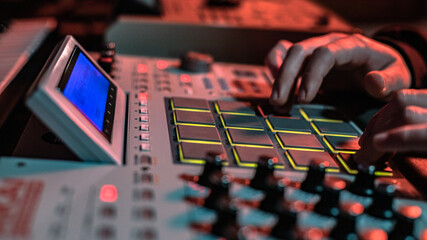 The hands of an artist creating music with his drum machines under red light.