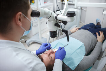 Naklejka na ściany i meble Mature man having dental treatment at the clinic, dentist using microscope