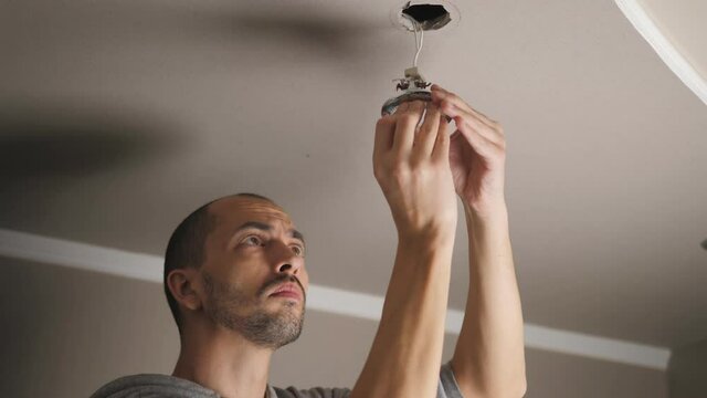 A young man is repairing a ceiling soffit. Replacing the LED lamp at the downlight