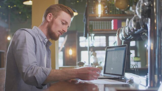 Male owner or manager of bar working at laptop on counter - shot in slow motion