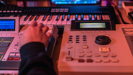 The hands of an artist creating music with his drum machines under red light.