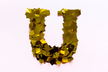 on a pink background of gold stripes of confetti a volumetric letter of the English and Russian alphabet U © Volha