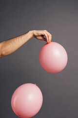 Close up of a man hand holding pink balloon on a grey studio background.