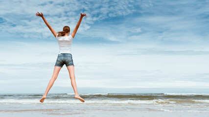 Obraz premium Happy girl jumping on the beach at day time- against blue sky