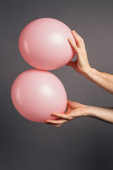 Close up of a man hand holding pink balloon on a grey studio background.