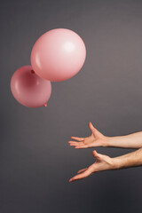 Close up of a man hand holding pink balloon on a grey studio background.