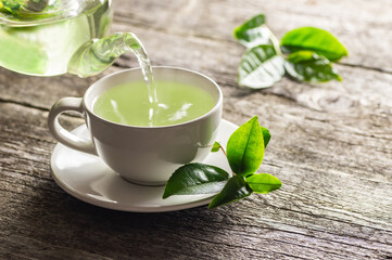 White cup of green tea with fresh tea leaves on wooden table, hot drink concept