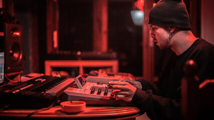 A producer in his studio, creating beats with his drum machines. Under red lights.
