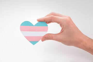 Hand holding a paper heart with transgender flag on white background
