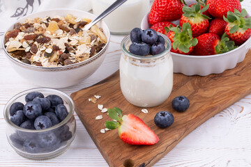 Healthy breakfast with homemade yoghurt and fresh strawberries and blueberries, muesli on a white wooden table in rustic style, close up, horizontal