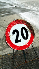20km speed limit construction site sign, damaged by time on asphalt seen from above