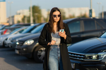 Car sharing, a young woman with a mobile phone in her hand near the Parking lot.
