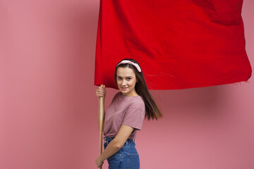 Young and beautiful girl with a red flag on a pink background. A socially active woman, to protest...