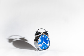 Un reloj de cuerda antiguo de color azul con su sombra detrás sobre un fondo blanco