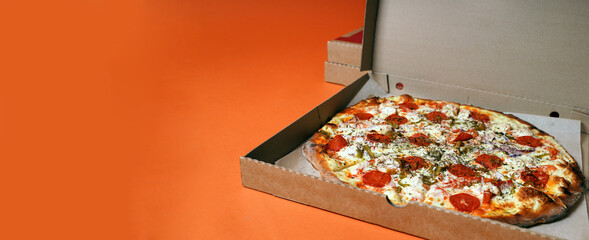 Close up of large pizza in box on orange background. Appetizing pizza with different ingredients.