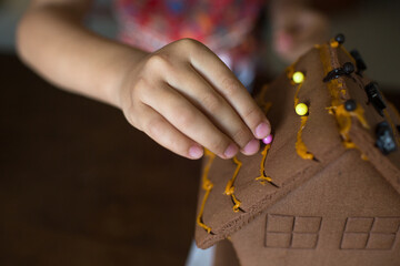 Hand of a girl making gingerbread house for Halloween.