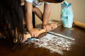 Brother and sister preparing chocolate cookies together. Teamwork to roll out the dough with the...