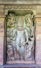 Aihole, Karnataka, India - November 7, 2013: Durga Gudi or Temple. Gray stone statue of male god with 6 arms and surrounded by six dancing women. 