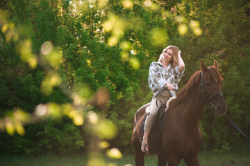 Woman with long hair posing with a brown horse in a forest in a sunny meadow.