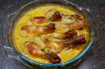 chicken drumsticks baked in sour cream sauce in a glass dish, on top of the meat is a fried crust