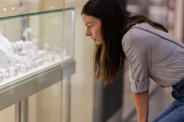 A young woman in a store admires a display of jewelry with diamonds and precious stones.