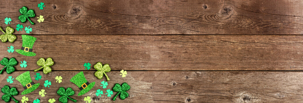 St Patricks Day shamrock and leprechaun hat corner border. Above view over a rustic wood banner background with copy space.