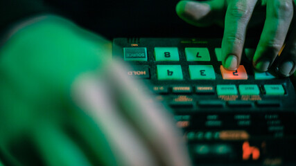 The hands of an artist creating music with his drum machines under green light.