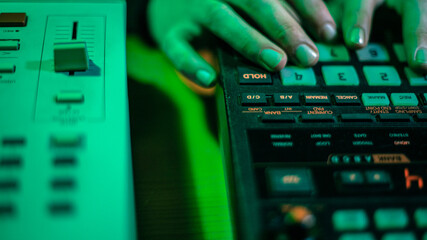 The hands of an artist creating music with his drum machines under green light.