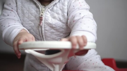 Childhood, entertainment, games, transport, motherhood concepts - active happy smiling joyful chubby infant baby kid child 10 months play ride big toy plastic red car scooter and beeps at home indoors