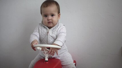 Childhood, entertainment, games, transport, motherhood concepts - active happy smiling joyful chubby infant baby kid child 10 months play ride big toy plastic red car scooter and beeps at home indoors