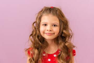 A little girl with curly hair smiles on a purple background.