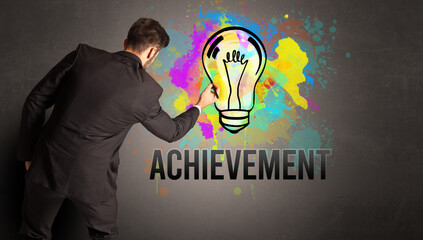 businessman drawing colorful light bulb with ACHIEVEMENT inscription on textured concrete wall, new business idea concept