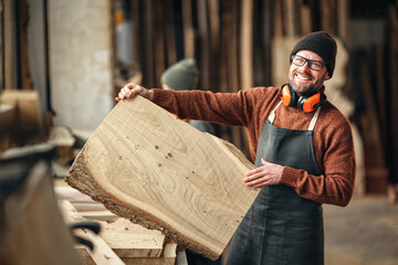 Happy carpenter with wooden board in workshop - obrazy, fototapety, plakaty
