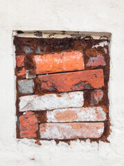 old square window filled with bricks. White wall