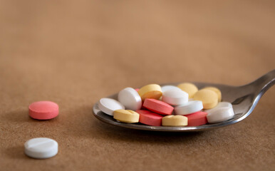 Close up of a spoon full of pink, white and yellow tablets on light brown background