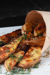 Tasty potato wedges wrapped into brown kraft wrapping paper. Fast food take away. Fried potatoes at rustic wooden boards background. Potatoes at stone. Fried chips, potato slices. Top view