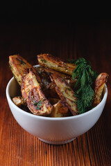 Delicious baked country potatoes in a clay bowl with spices, dill and green onions, on a wooden table, space for text