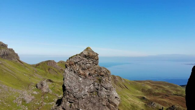 A reverse aerial clip of the Old Man of Storr in the Isle of Skye on a clear sunny day in Scotland. From the center of the pinnacle, you can see tourists exploring the site