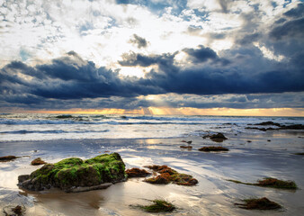 Obraz premium Light rays illuminate the Pacific Ocean beneath dark storm clouds at Crystal Cove State Park in Laguna Beach, California.