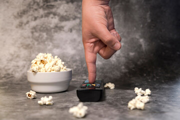 Bowl with popcorn, man's hand with TV remote control on dark background