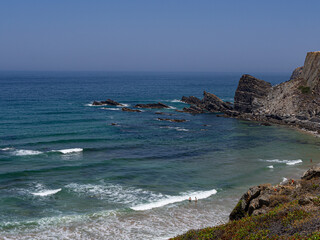 People in empty beach with waves and blue water, paradise, in costa vicentina, alentejo, portugal