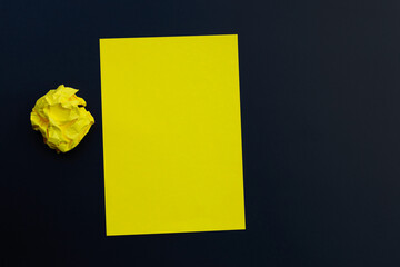 Yellow sheet with crumpled paper ball on dark background.