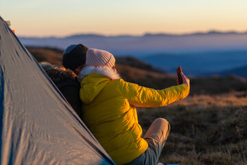 Portrait of a young couple taking a selfie with a phone in the mountains next to their tent.