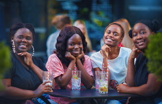 A Group Of Beautiful Happy African American Women, Girls Chilling Out At Summer Outdoor Cafe, Drinking Cocktails And Having Fun