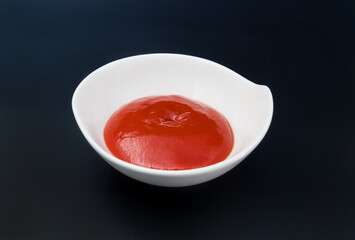 Red Souce in white dish on black, dark background